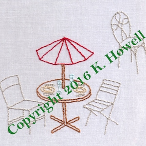 May include: Embroidered design of a red umbrella over a table with three chairs, two of which are white and one is brown. The table has a brown base and a white top with a brown rim. The design includes the text "Copyright 2016 K. Howell".