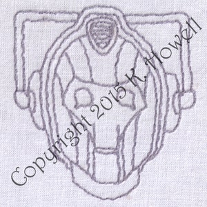 May include: A gray embroidered design of a robot head with a circular shape and a face with a single eye. The text "Copyright 2015 K. Howell" is visible in the lower left corner of the image.