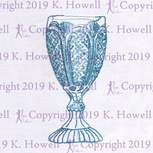Puede incluir: Un diseño bordado en azul y blanco de una copa con tallo y un patrón decorativo. El diseño está sobre un fondo de tela blanca.