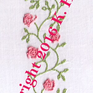 May include: Embroidered design of a pink rose plant in a brown pot with green leaves and stems. The text "Copyright 2016 K. Howell" is diagonally across the image.