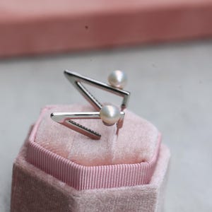 May include: A pair of silver earrings with a geometric triangle design and a white pearl accent on each earring.