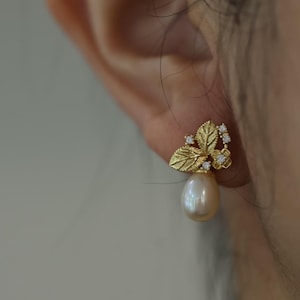 Puede incluir: Pendientes de oro con una perla colgante y un delicado diseño de hojas y diamantes.