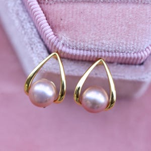 May include: A pair of gold earrings with a teardrop shape and a single pink pearl in each earring.