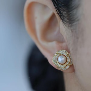 Puede incluir: Pendientes de oro en forma de flor con un centro de perla y piedras de circonita cúbica transparentes.