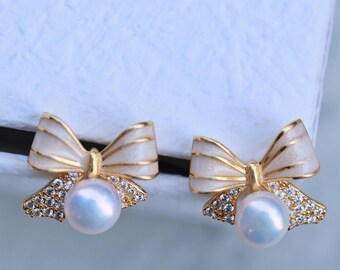 May include: A pair of gold-tone earrings with a white enamel bow and a pearl drop. The bows are accented with clear cubic zirconia stones.