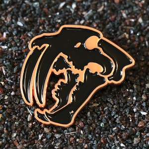 Può includere: Uno spillo in smalto nero e rame con una silhouette dettagliata di un cranio di tigre dai denti a sciabola.