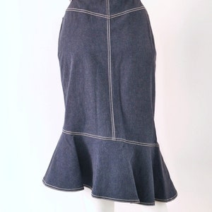 May include: A dark blue denim skirt with a white stitched trim. The skirt has a flared hem and a colorful braided belt.