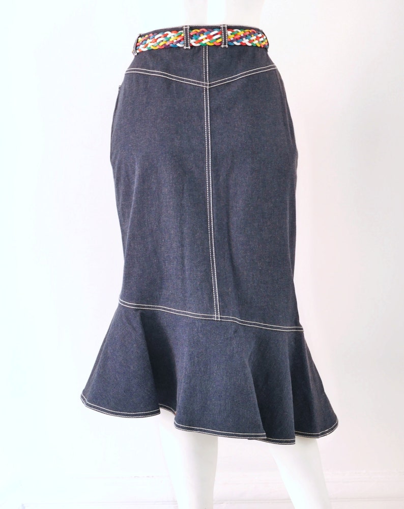 May include: A dark blue denim skirt with a white stitched trim. The skirt has a flared hem and a colorful braided belt.