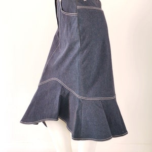 May include: A dark blue denim skirt with a flared hem and white stitching. The skirt has a high waist and a fitted silhouette.