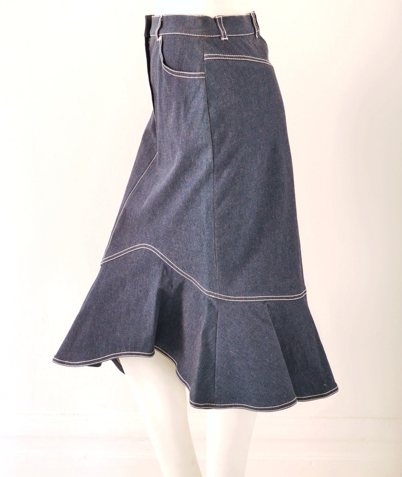 May include: A dark blue denim skirt with a flared hem and white stitching. The skirt has a high waist and a fitted silhouette.