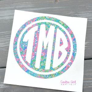 May include: A white decal featuring a circular design with the initials "TMB" in a bold, white font. The circle is filled with a colorful pattern of pink, blue, and green swirls. The text "Carolina Girl Sawtique" is at the bottom.