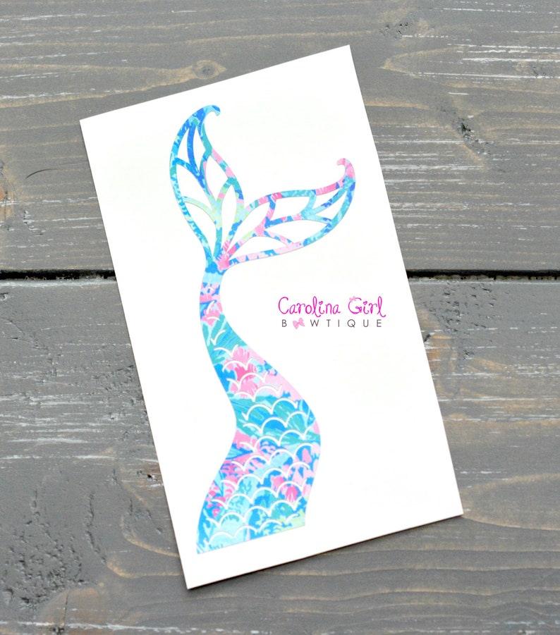 May include: A white card features a colorful mermaid tail design. The tail is a mix of blue, pink, and green patterns. The text "Carolina Girl BWTiQUE" is printed in pink on the card.
