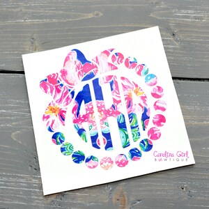 May include: A white sticker featuring a floral monogram design in pink, blue, and green. The monogram is surrounded by a circle of smaller floral circles. The text "Carolina Girl Bowtique" is printed in the lower right corner.