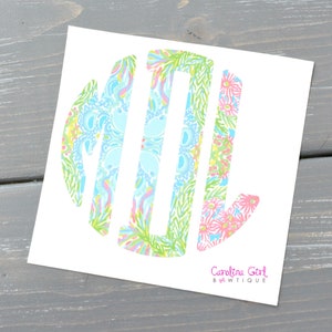 May include: A white sticker with a monogram design. The monogram features the letters MTL in a circular arrangement, filled with colorful floral and paisley patterns in shades of blue, pink, green, and yellow. The text "Carolina Girl BWTiQUE" is printed in pink.