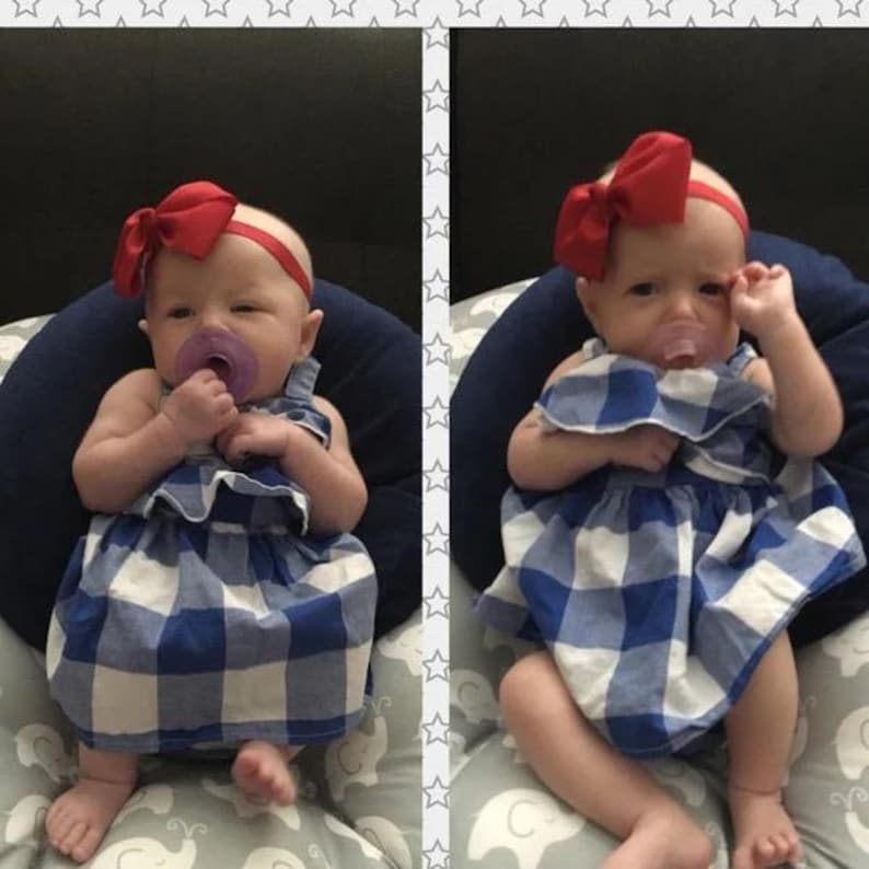 Pu&ograve; includere: Un bambino che indossa un vestito a quadri blu e bianchi con un cerchietto rosso con fiocco e un ciuccio. Il bambino &egrave; seduto su un cuscino con motivo grigio e bianco.