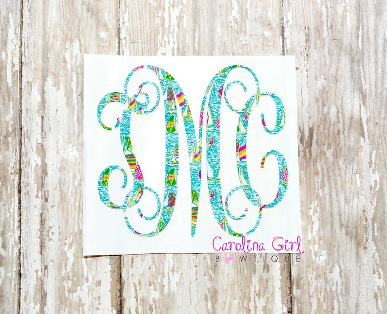 May include: A white decal featuring a monogram with the letters "DMC" in a decorative script. The letters are filled with a colourful pattern of sailboats on a turquoise background. The text "Carolina Girl BWTiQUE" is below the monogram.
