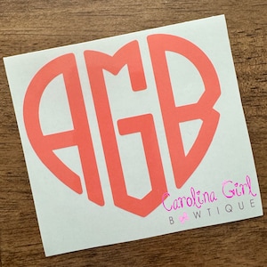 May include: A coral-colored monogram sticker in a heart shape, featuring the letters "AGB". The sticker is on a white background, with the text "Carolina Girl Bowtique" in pink script at the bottom.
