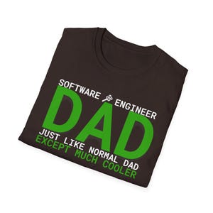Könnte beinhalten: Ein dunkelbraunes T-Shirt mit dem Text "Software Engineer Dad" in Weiß und Grün. Der Text "Just like normal dad except much cooler" ist ebenfalls in Weiß auf dem T-Shirt aufgedruckt.