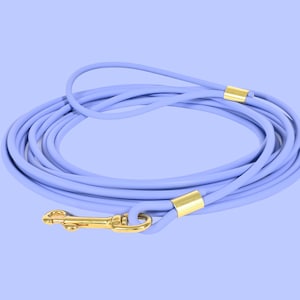 May include: A coiled lavender dog leash with gold-colored metal accents. The leash has a loop handle and a gold-colored clasp. The leash is made of a soft, flexible material. The background is a light purple color.
