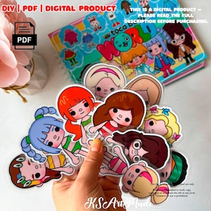 May include: A collection of die-cut stickers featuring cartoon characters with diverse hair colors and styles, including blue, orange, brown, and blonde. The stickers are held in a hand, with a Toca Boca World digital product notebook visible in the background.