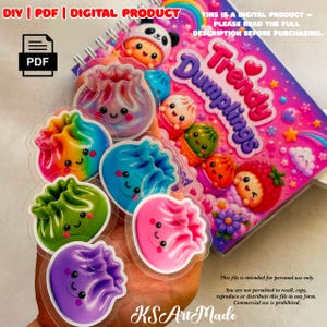 Può includere: Un prodotto digitale che include un quaderno a spirale con copertina rosa intitolata Trendy Dumplings, circondato da diversi adesivi colorati di ravioli sorridenti nelle tonalità viola, verde, blu, arcobaleno e rosa con finitura lucida.