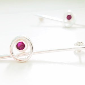 Può includere: Un paio di orecchini d'argento con un'unica pietra rosa incastonata in un cerchio. Gli orecchini sono lunghi e sottili, con un design semplice.