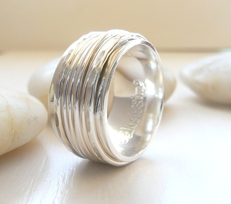 K&ouml;nnte beinhalten: Ein silberner Ring mit geh&auml;mmerter Textur und mehreren B&auml;ndern. Der Ring ist breit und hat eine abgerundete Form.