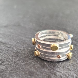 May include: A silver ring with multiple bands and gold accents. The ring is decorated with small gold dots.