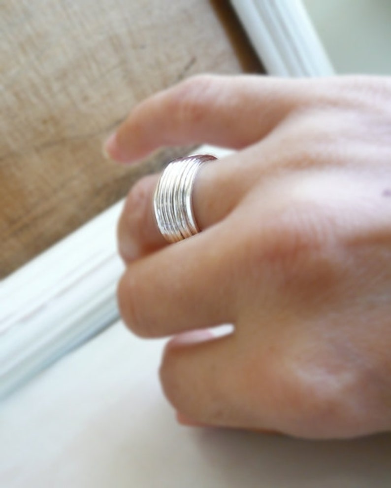 K&ouml;nnte beinhalten: Ein Stapel silberner Ringe, die an einem Finger getragen werden.