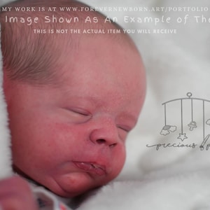 Może przedstawiać: Zbliżenie twarzy noworodka z zamkniętymi oczami i lekko otwartymi ustami. Dziecko jest owinięte w biały kocyk. Obraz zawiera tekst: "This Image Shown As An Example of The Kit". Widoczne jest również logo "precious paz".