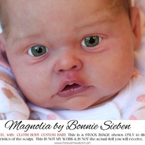 Może przedstawiać: Zbliżenie lalki dla dziecka z zielonymi oczami i lekko otwartymi ustami. Lalka ma na sobie biało-różowe body we wzory. Tekst "Magnolia by Bonnie Sieben" znajduje się na dole obrazu.