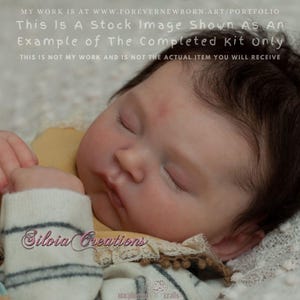 Könnte beinhalten: Eine realistische Reborn-Puppe mit geschlossenen Augen und dunkelbraunem Haar. Die Puppe trägt ein gelbes Kleidungsstück und eine gestreifte Socke. Der Text "Silvia Creations" ist auf der Socke zu sehen. Das Bild ist ein Stockfoto-Beispiel.