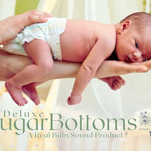 Può includere: Un neonato con il pannolino è tenuto delicatamente tra le mani di qualcuno. Il bambino è sdraiato su un fianco, con la testa appoggiata sul palmo della mano. L'immagine include il testo "Deluxe Sugar Bottoms" e "A Real Baby Sound Product".