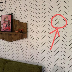 May include: A small, white, ghost-shaped wall hook mounted on a wall with a black and white herringbone pattern. The hook features a simple, rounded top and a narrow base, designed for hanging lightweight items securely against the patterned surface.