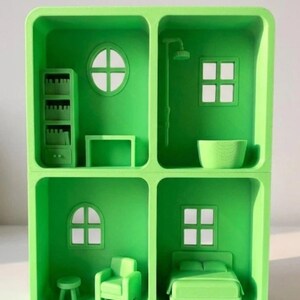 May include: A bright green miniature dollhouse with four distinct rooms. Each room features small-scale furniture, including a bed, armchair, bookshelf, and shower. The windows are square or circular, and the overall design is minimalist and modern.