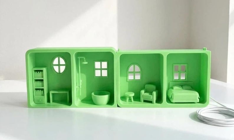 May include: A lime green miniature dollhouse with four rooms. The rooms include a bathroom with a shower and tub, a living room with a chair and table, and a bedroom with a bed. The dollhouse has a white cord.