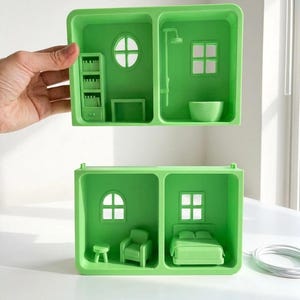 May include: Two-part green dollhouse with miniature furniture. One section features a bookshelf, round window, and table. The other section has a shower, square window, and bowl. The second dollhouse has a chair, bed, and stool.