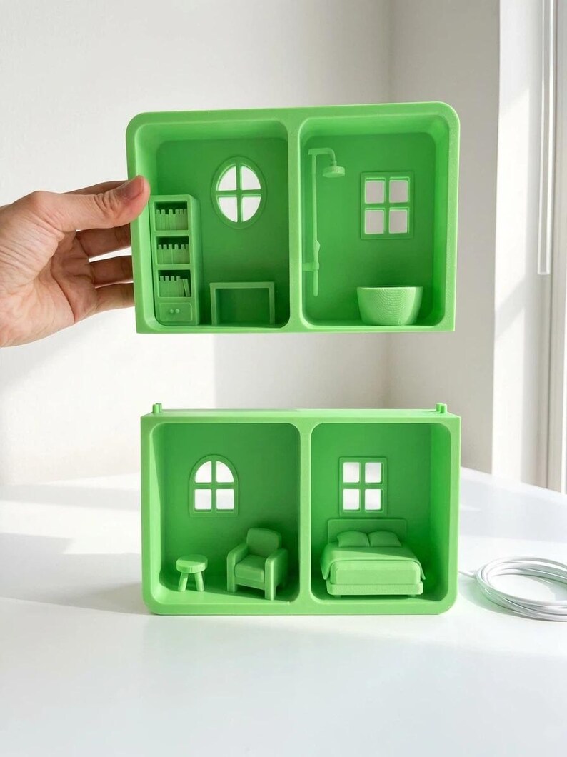May include: Two-part green dollhouse with miniature furniture. One section features a bookshelf, round window, and table. The other section has a shower, square window, and bowl. The second dollhouse has a chair, bed, and stool.