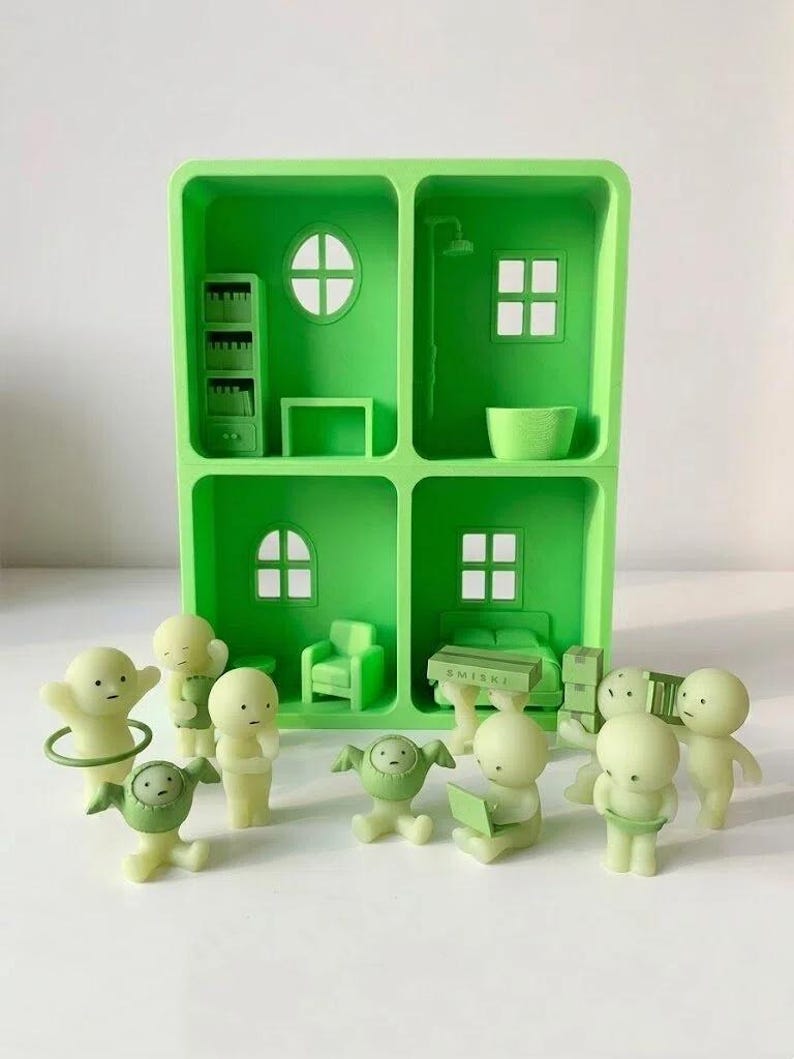 May include: A green dollhouse with four rooms, each with miniature furniture and windows. Several small, light green figurines are scattered around the dollhouse, some holding objects. The dollhouse and figurines are made of plastic.
