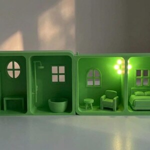 May include: A green miniature dollhouse with four rooms, each illuminated with a soft green light. The rooms include a bathroom, bedroom, and living room, with miniature furniture and fixtures. A white cord is visible.