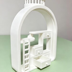 May include: A white, architectural-style decorative piece featuring an arched frame. Inside, there's a miniature ladder, shelves, and several small drawers, one of which is open. The top has a decorative, column-like design.