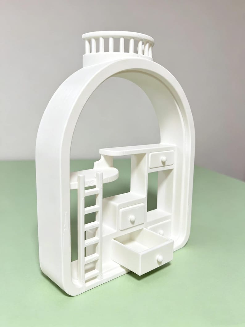 May include: A white, architectural-style decorative piece featuring an arched frame. Inside, there's a miniature ladder, shelves, and several small drawers, one of which is open. The top has a decorative, column-like design.