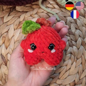 Puede incluir: Un juguete de peluche rojo hecho a mano con forma de estrella con detalles verdes y naranjas. El juguete tiene ojos negros y detalles blancos. El texto "Miss Blue Buttons" está escrito en la parte inferior del juguete.