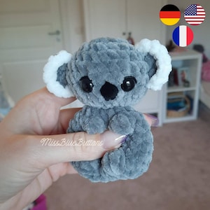 Könnte beinhalten: Ein handgemachter grauer und weißer Koala-Bär aus Plüsch. Der Koala hat große schwarze Augen, eine schwarze Nase und weiße, flauschige Ohren. Das Plüschtier ist aus weichem, strukturiertem Material gefertigt. Der Text "Miss Blue Buttons" ist sichtbar.