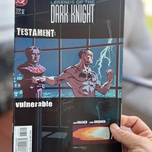 May include: A comic book cover for "Batman: Legends of the Dark Knight" #175. The cover features a muscular figure with a lightning bolt and the word "vulnerable". The title "Testament" is also visible.