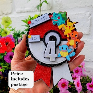May include: A circular badge designed like a Poké Ball with a red top and white bottom, featuring the text ROSIE IS and a large number 4 in the center. The badge is decorated with small cartoon figures of Bulbasaur, Pikachu, Charmander, and Squirtle.