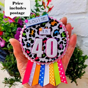 May include: A handmade birthday badge with a leopard print design, featuring the number 40 in silver glitter. The badge includes colorful ribbons and the name "Louise". A fun and festive accessory for a milestone birthday celebration.