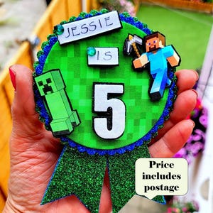 May include: A Minecraft-themed birthday badge in green and blue, featuring the name "Jessie" and the number "5". The badge includes a Creeper and a pixelated design. It has a green glitter ribbon and a blue and green border.