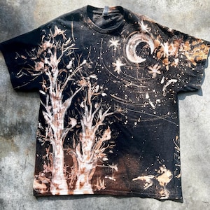 Puede incluir: Camiseta negra con un diseño de teñido con lejía que presenta dos árboles y una luna creciente con estrellas en el cielo nocturno.