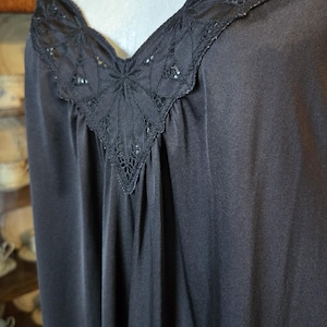 May include: Black slip dress with delicate spaghetti straps and a V-neckline. The neckline is adorned with intricate lace detailing. The dress is made of a smooth, flowing fabric, creating an elegant silhouette. A classic piece for sleepwear or layering.